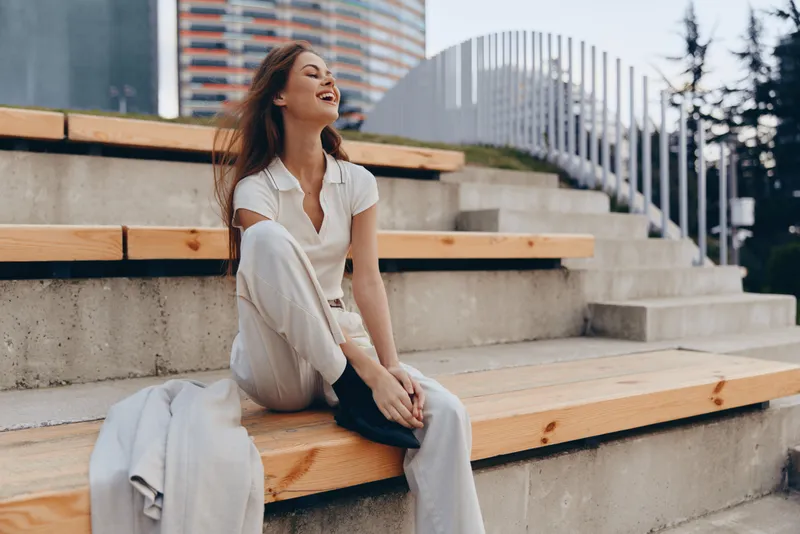 happy woman in white casual outfit laughing outdoors on wooden stairs urban background fashion lifestyle spring season