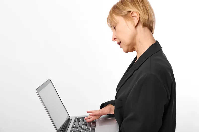 Stressed woman using laptop in side view on white background, office technology concept, worried expression, remote work anxiety, productivity pressure