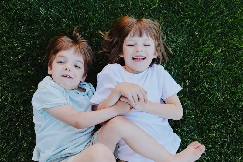 Happy children laughing together on green grass, showcasing their joy and playful spirit in a vibrant outdoor setting under the sun.