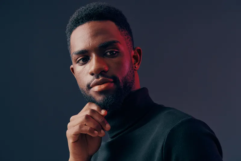 Young African man in black turtleneck sweater posing confidently against a dark background, conveying a strong and thoughtful emotion