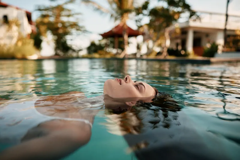 Relaxed swimmer floating on back in a sunlit pool, serene expression, clear water reflections, tropical resort vibe, casual summer mood, gentle breeze, vibrant colors