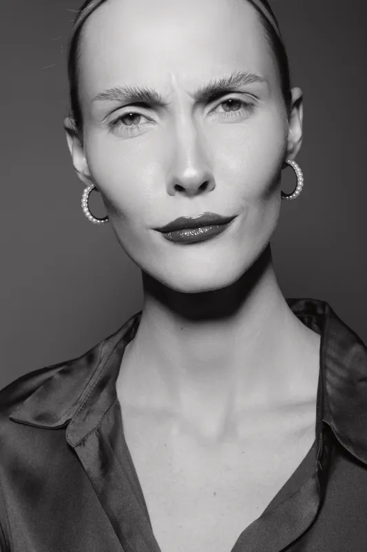 Portrait of a serious Caucasian woman with pale skin and slicked-back hair wearing pearl hoop earrings and a dark blouse. Concept of elegance, confidence, and fashion portrait.