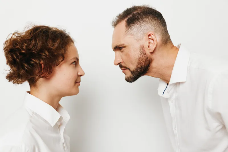 A professional man and colleague face off with focused emotion, isolated on a plain background, conveying business tension, dialogue, and purposeful interaction.