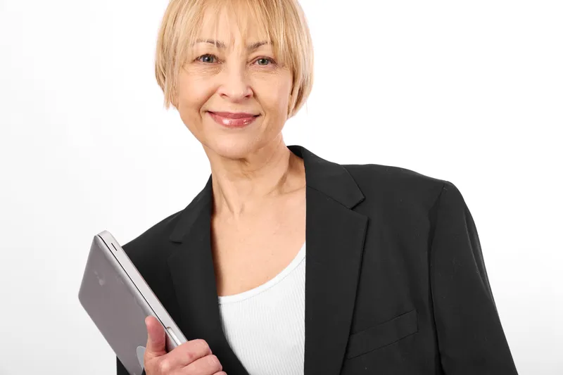 Senior woman in business blazer holding a book, smiling in studio portrait against clean white background, professional confident mood, copy space for work