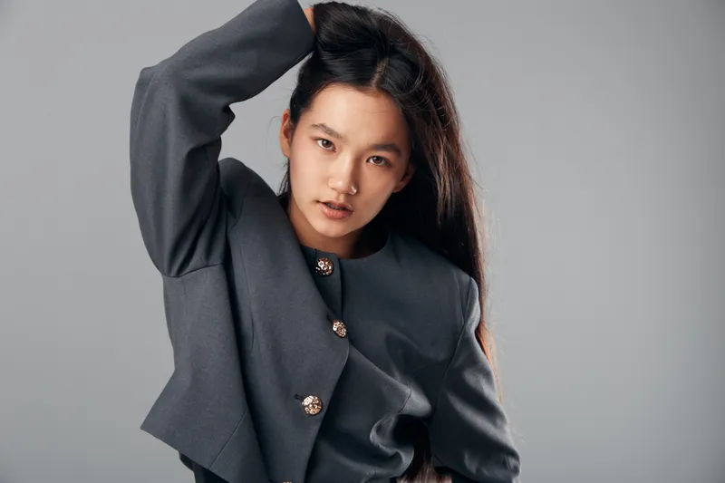 Portrait of young woman posing with hand in hair wearing gray stylish jacket with decorative buttons on neutral background for fashion and beauty concept.