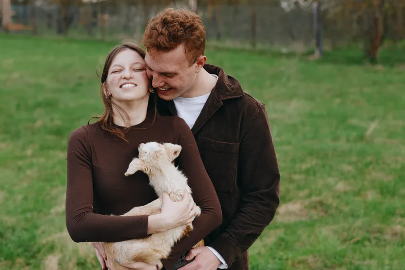 A joyful couple hugs their small dog in a sunny park, capturing warmth, affection, and everyday companionship outdoors, ideal for lifestyle and pet bonding concepts.
