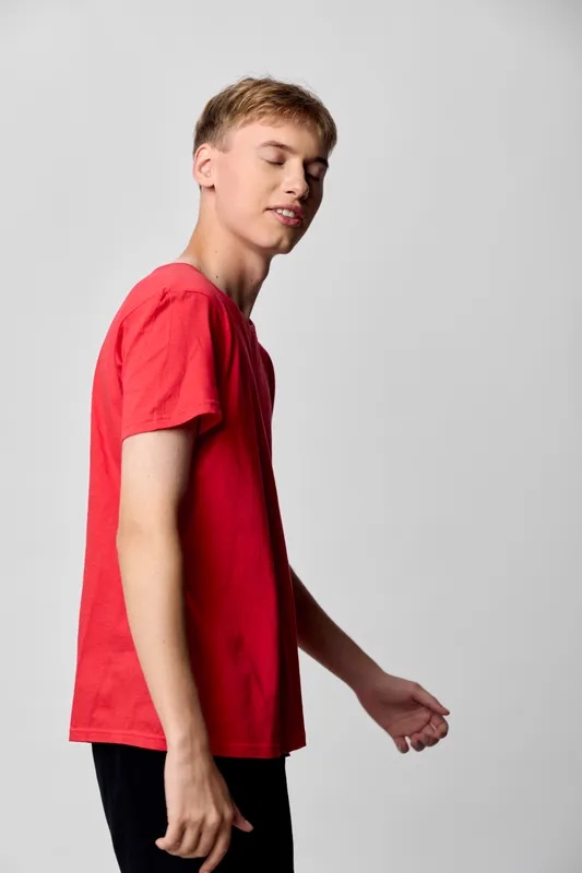 Teen boy in a red shirt standing in a simple studio setting, casual pose and relaxed attitude, bright lighting highlights fabric texture, posture exudes confidence, minimal backdrop, clean commercial