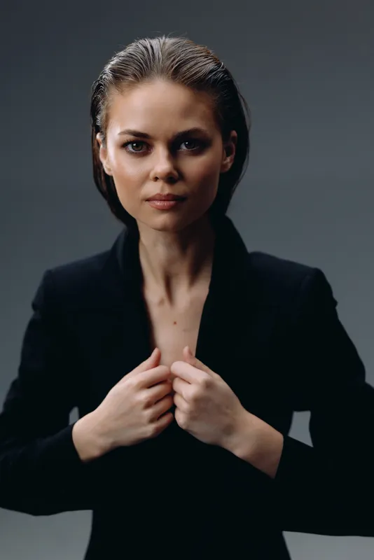 Confident woman in black jacket posing with serious expression against dark background