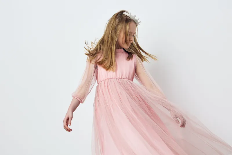 Elegant young girl in a flowing pink dress twirling joyfully against a clean white background, showcasing beauty, innocence, and grace in a seasonal portrait