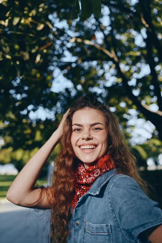 Lifestyle woman in modern boho-western denim street style smiling outdoors with natural light and film color effect, casual red bandana accessory.