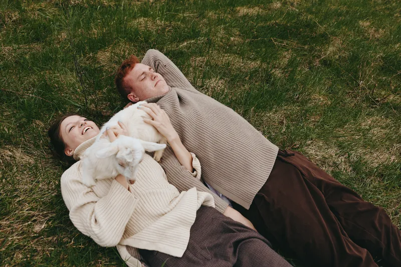 couple lifestyle outdoor pastoral goat kid grass relaxation companionship nature a carefree moment with a playful goat kid and two people smiling on a sunny meadow, capturing wholesome rustic family