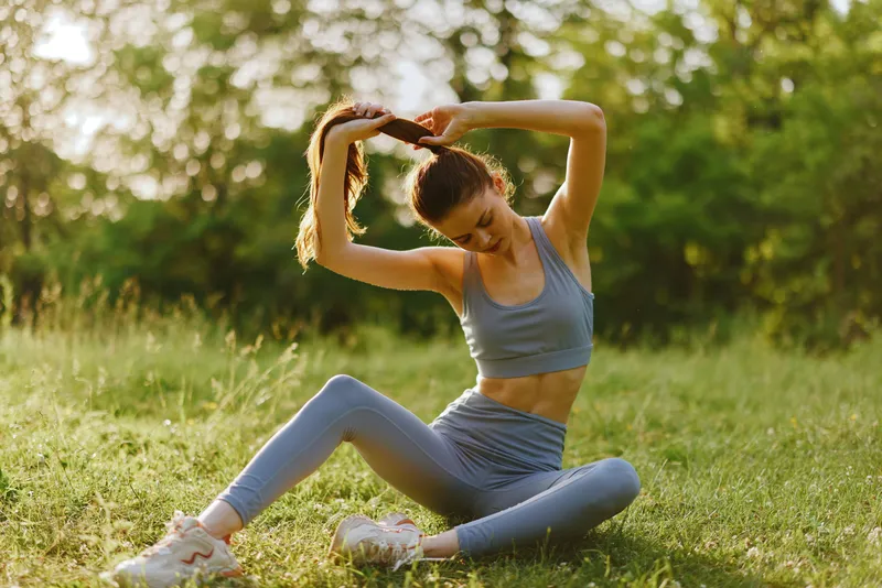 Young woman practicing yoga outdoors in a green park, wearing sporty attire and showing a focused expression while stretching her body