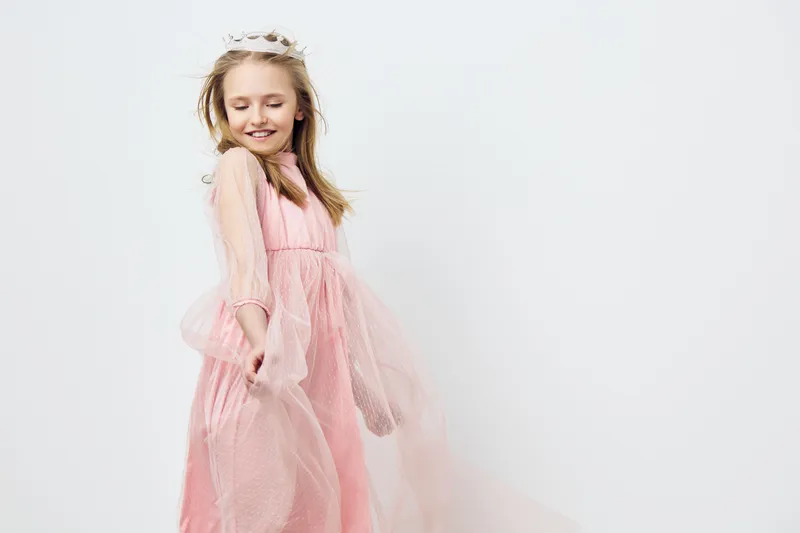 A joyful little girl in a pink dress with tulle, dancing gracefully against a soft white background, conveying happiness and innocence in her expression