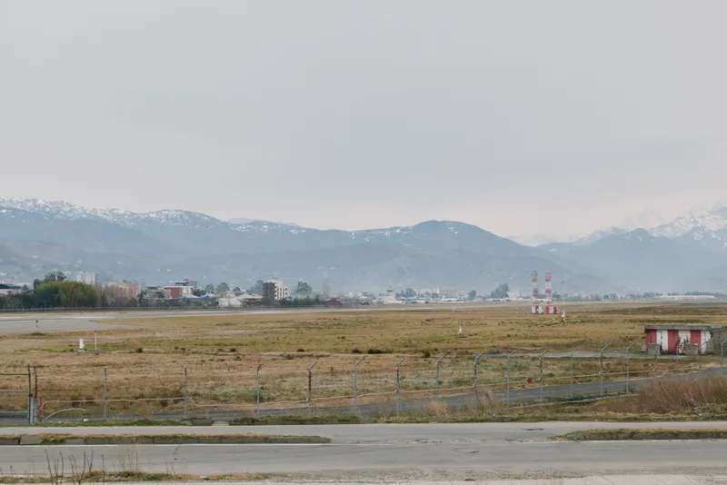 Empty airfield with runway and small buildings in front of hazy mountains under cloudy sky. Concept for aviation, transportation, and industrial landscape with wide open space.