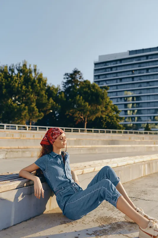 Lifestyle woman in modern boho-western denim street style relaxing outdoors with a film color tone, enjoying warm sunlight and casual urban environment.