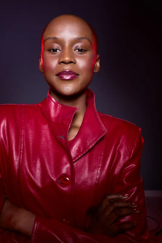 Confident dark skinned African woman wearing a shiny red leather jacket poses with arms crossed against a dark background. Concept of empowerment, fashion, and style.