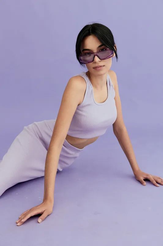 young woman wearing purple sunglasses and matching outfit posing on lavender background, stylish casual look with confident expression and modern vibe