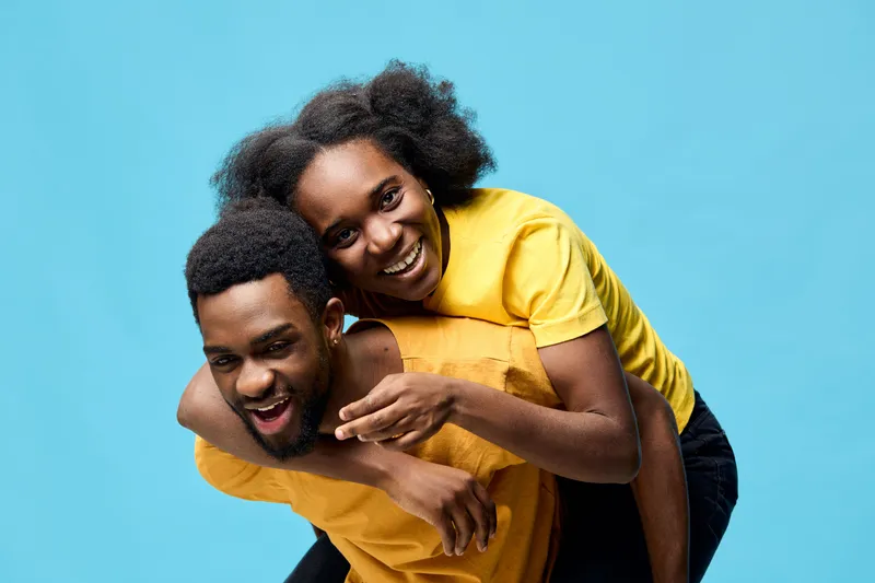 Joyful couple enjoying playful moment, wearing bright yellow outfits on vibrant blue background, representing fun, happiness, and love in a seasonal theme
