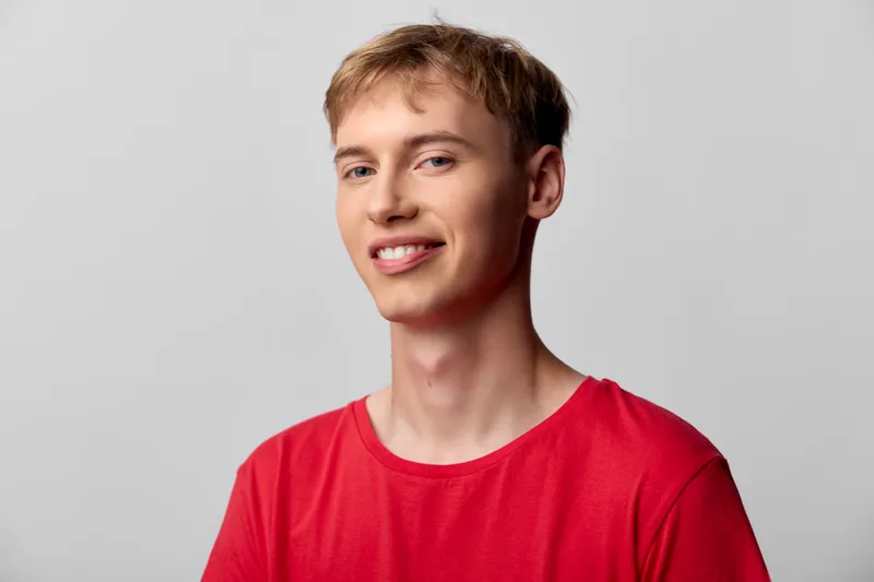Smiling man in a red shirt, casual studio setup with a clean background and soft lighting, conveying friendly energy and contemporary fashion for lifestyle and marketing visuals