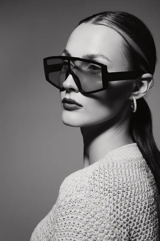 Portrait of a white woman with pale skin wearing large sunglasses and hoop earrings in black and white.