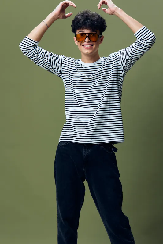 smiling young man wearing yellow sunglasses and striped shirt showing heart gesture with hands against olive green background, casual, joyful, playful mood