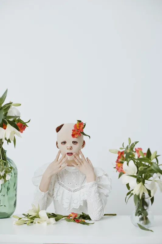 Artistic portrait of a model with a unique mask, surrounded by colorful flowers, embodying themes of identity and nature, perfect for contemporary art projects