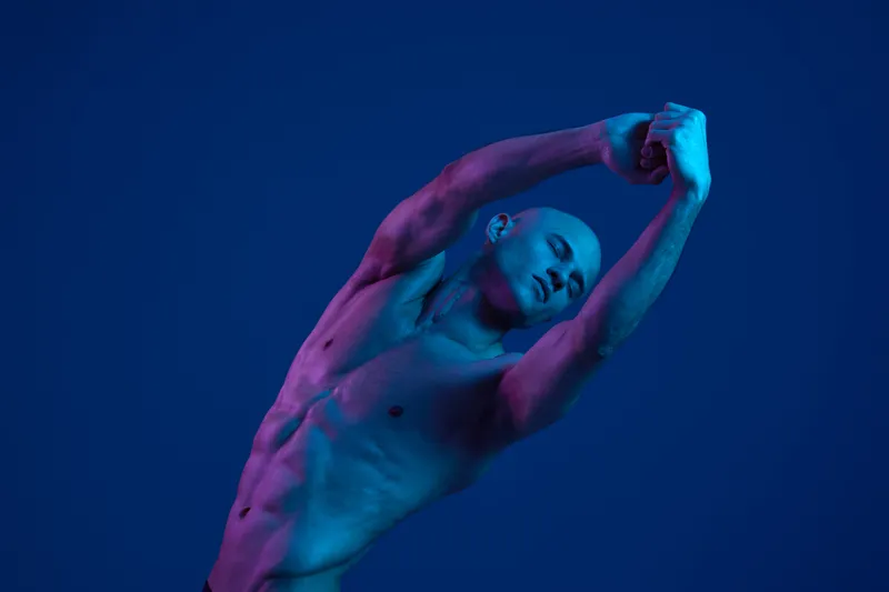 A striking image of a man performing a graceful dance pose, showcasing athleticism and expression in a bold blue and purple light. Perfect for dynamic art themes.