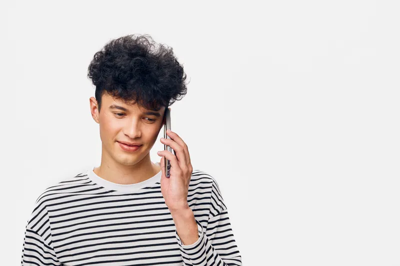 Young man using smartphone, talking and smiling, casual striped shirt, curly hair, isolated on white background, technology communication concept.