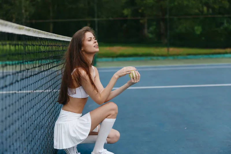 Young woman in athletic wear poses thoughtfully on a tennis court, embodying focus and determination in a vibrant outdoor setting, with a seasonal sports theme