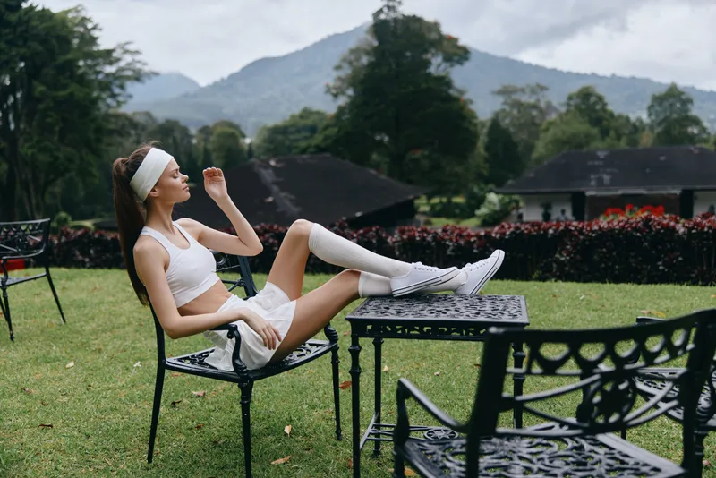 Young woman relaxing in sporty attire on a chair outdoors with mountain view, portraying tranquility, health, and wellness in nature