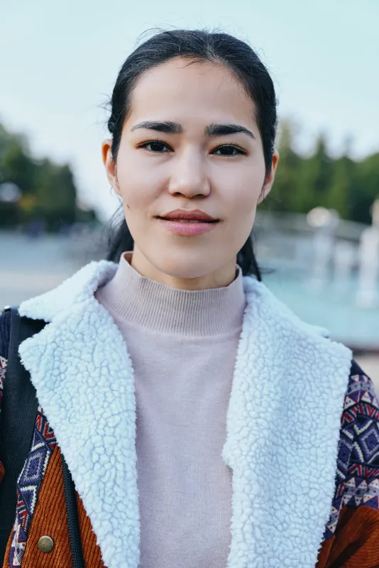 Woman wearing a cozy fleece-lined coat standing outdoors with a calm confident expression, showcasing casual streetwear and everyday fashion in natural daylight