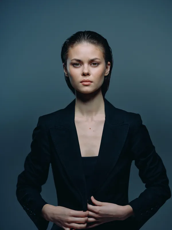 serious woman in black suit jacket with wet hair stands against dark background with focused expression