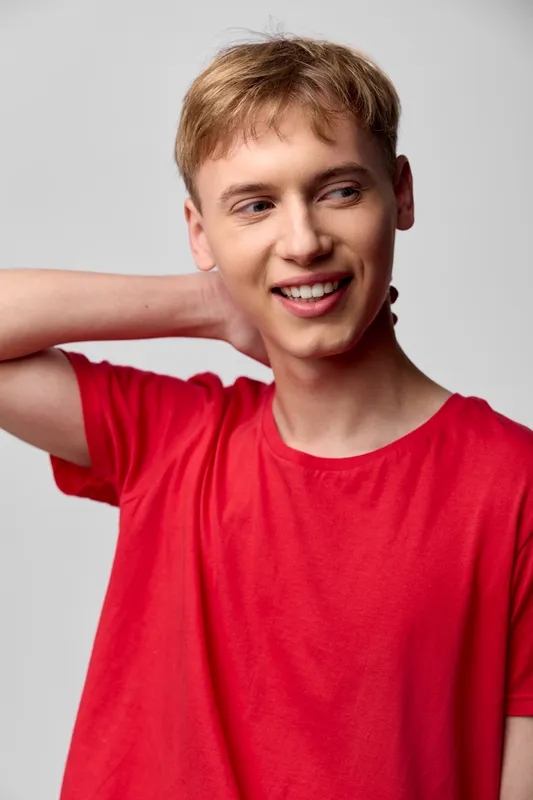 Smiling man in a red tshirt poses casually with a hand behind the neck in a bright studio, conveying relaxed lifestyle fashion and everyday confidence for lifestyle or fitness projects
