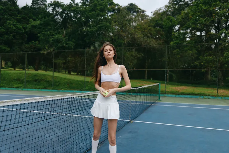 Young female tennis player in stylish white sportswear on a lush green tennis court, expressing determination and focus, perfect for sports related content