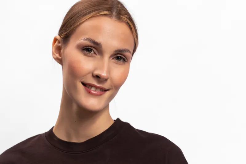 Smiling young woman with light brown hair and clear skin wearing black shirt isolated on white background. Portrait of happy female model with natural makeup and positive facial expression.