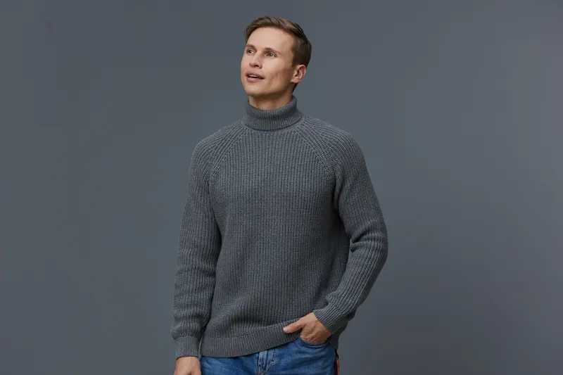 Casual mature man wearing cozy gray turtleneck sweater smiling and looking upwards isolated on plain gray background studio portrait. People lifestyle concept