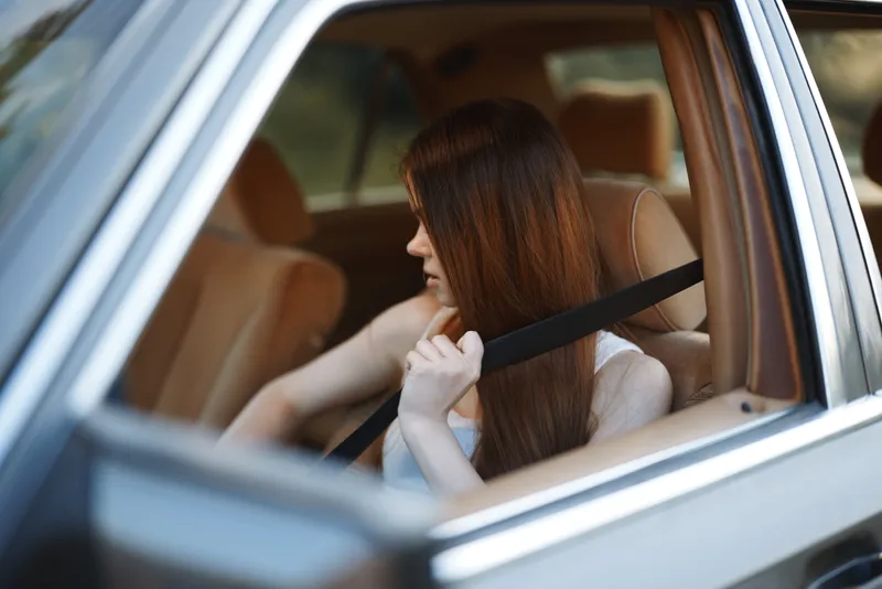 Young woman with long hair fastening her seatbelt in a car, conveying safety and comfort with a warm color palette.