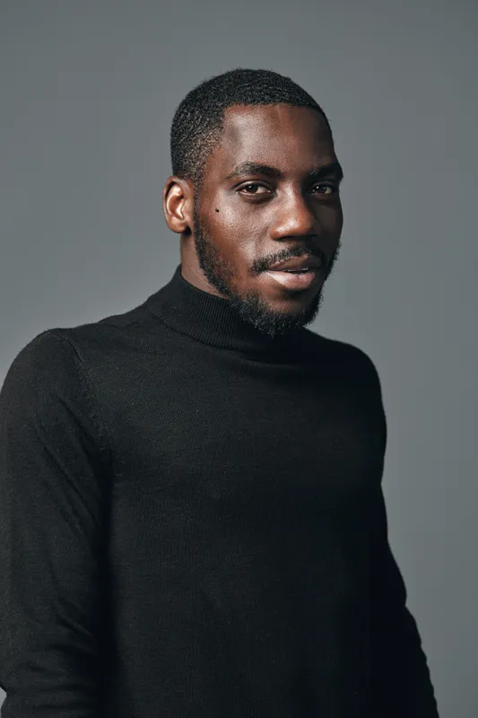 African man with dark skin wearing black turtleneck sweater posing in studio with neutral gray background creative conceptual visual style portrait of confident male model.