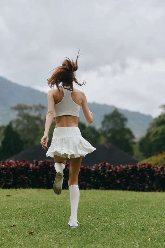 Young woman running in a sporty outfit on a lush green field, showcasing joy and freedom in a vibrant natural setting with mountains in the background