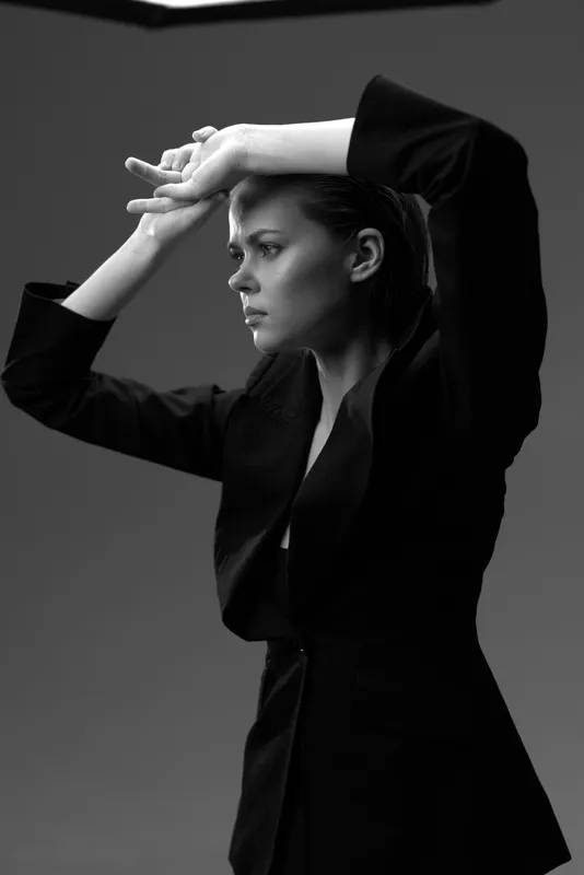 Black and white portrait of a serious woman in a blazer with raised arms expressing emotion and intensity.