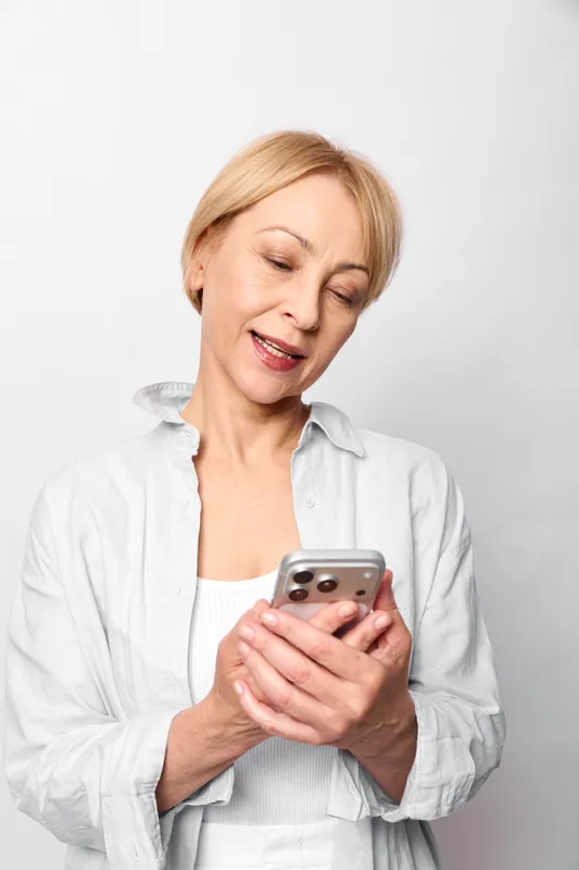 Woman smartphone worried communication mobile portrait texting anxiety, woman in white blouse looks concerned at phone, indoor studio portrait against plain background