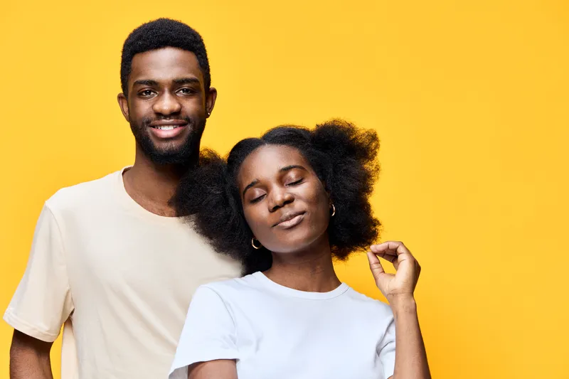 African couple with joyful expressions against a bright yellow background, showcasing love and confidence through their vibrant colors and relaxed outfits