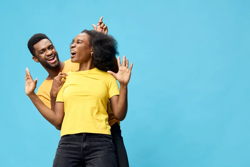 Joyful couple celebrating together in vibrant yellow outfits against a bright blue background, expressing happiness and connection through playful gestures