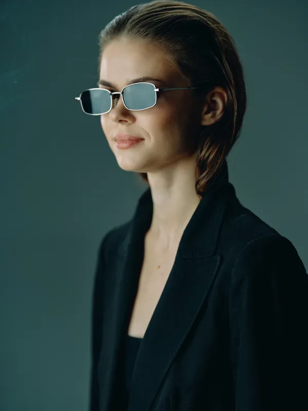 Stylish woman wearing modern sunglasses and a black blazer with a confident expression and sleek hairstyle.