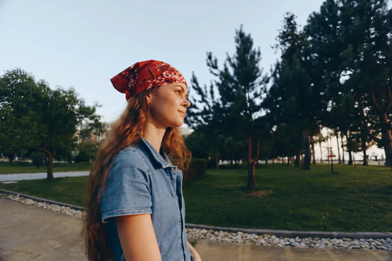 young woman wearing red bandana outdoors, thoughtful expression, casual denim shirt, green park background, natural light, peaceful atmosphere