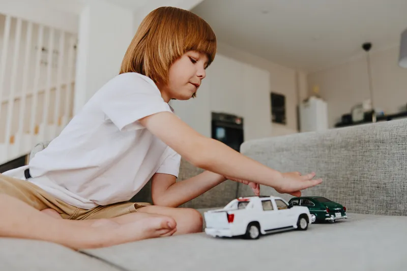 A playful boy engaging with toy cars, showcasing creativity and imagination in a cozy living room setting. Bright colors and joyful atmosphere enhance the scene.