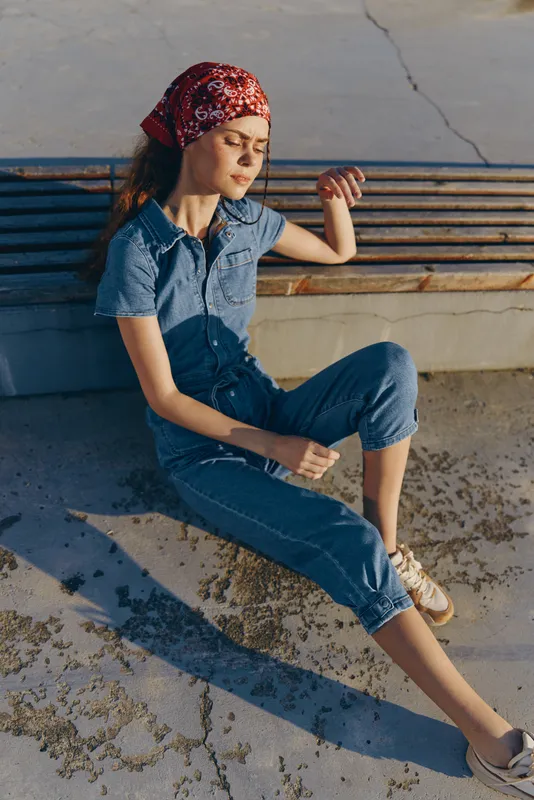 Lifestyle woman in modern boho-western denim street style sits relaxed outdoors in warm natural light with film color tone enhancing casual fashion vibe.