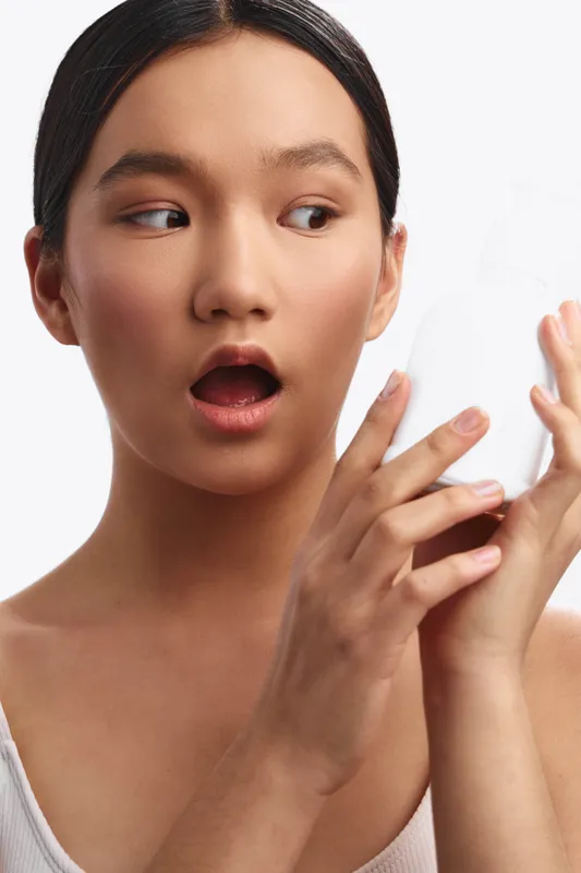 asian woman shows surprise as she examines her hands in a closeup shot, conveying curiosity and wonder in a clean studio setting. The soft lighting highlights smooth skin and calm expression,