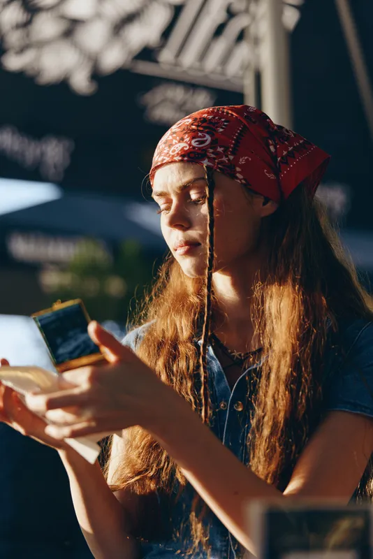 Lifestyle woman in modern boho-western denim street style with a red bandana, natural light, and film color capturing a casual, artistic moment outdoors.