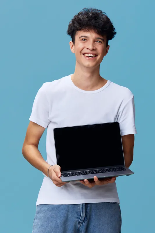 smiling man holding laptop in casual white t-shirt and jeans standing against blue background, technology, cheerful, young, modern